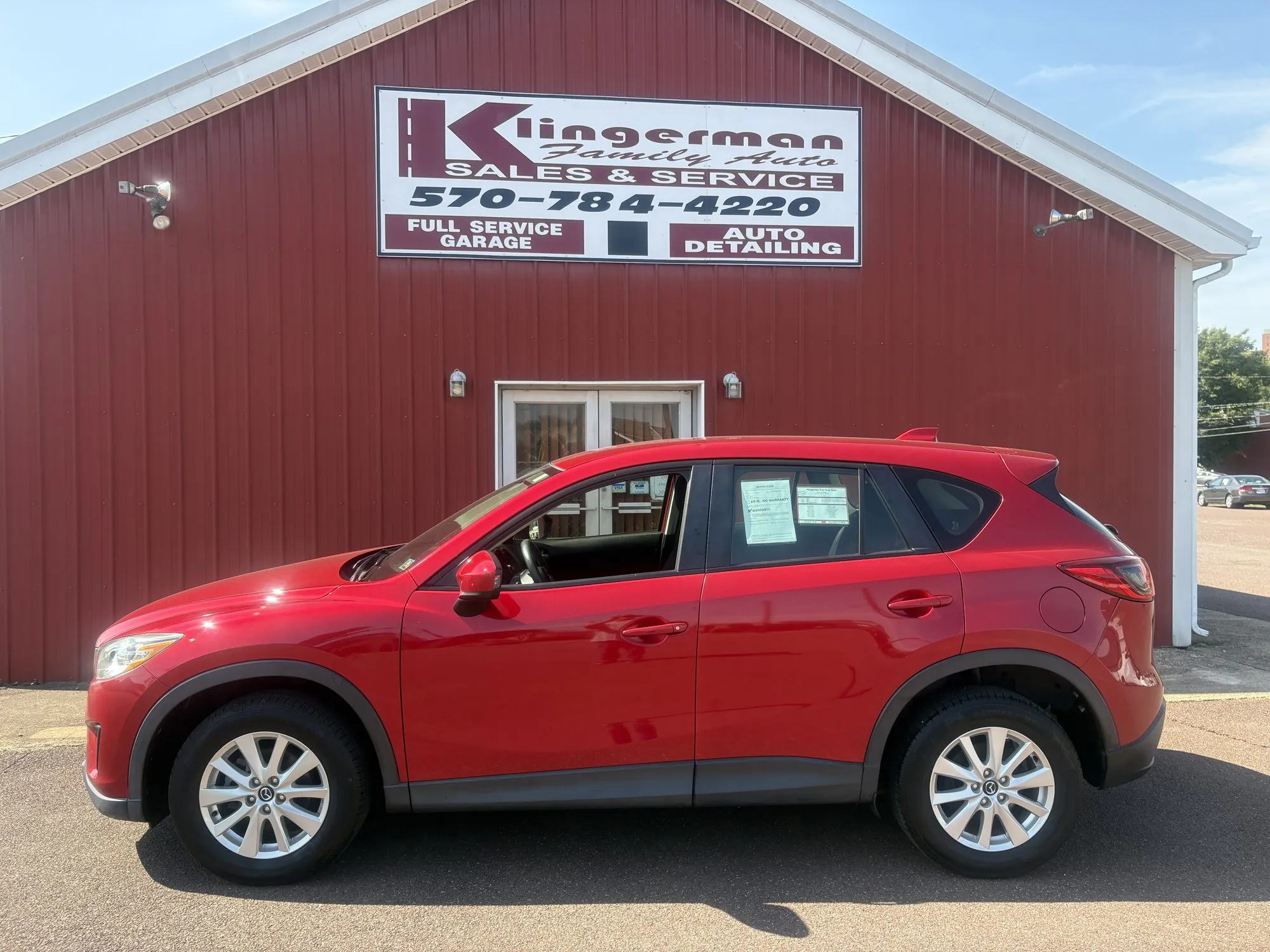 A red 2014 Mazda CX-5 Sport parked in front of the Klingerman Family Auto building