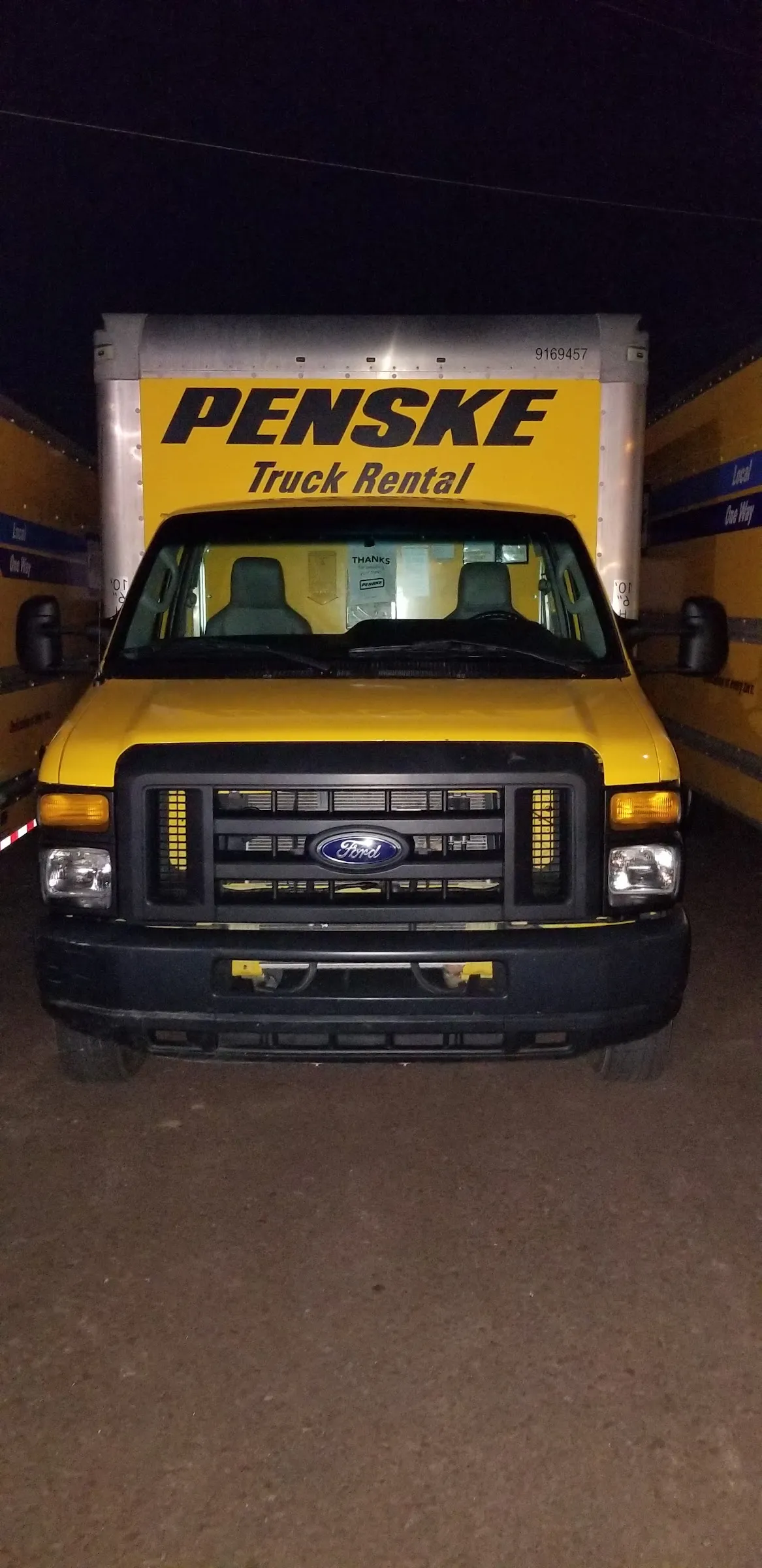 A Penske rental truck parked on a gravel lot at night, more trucks beside it